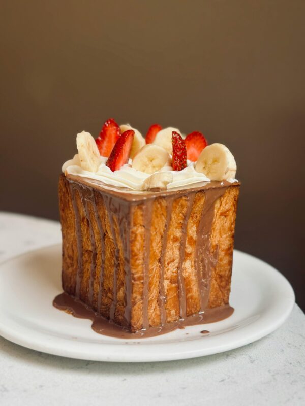 Close-up of a decadent Shibuya honey toast topped with banana, strawberry, and chocolate sauce.