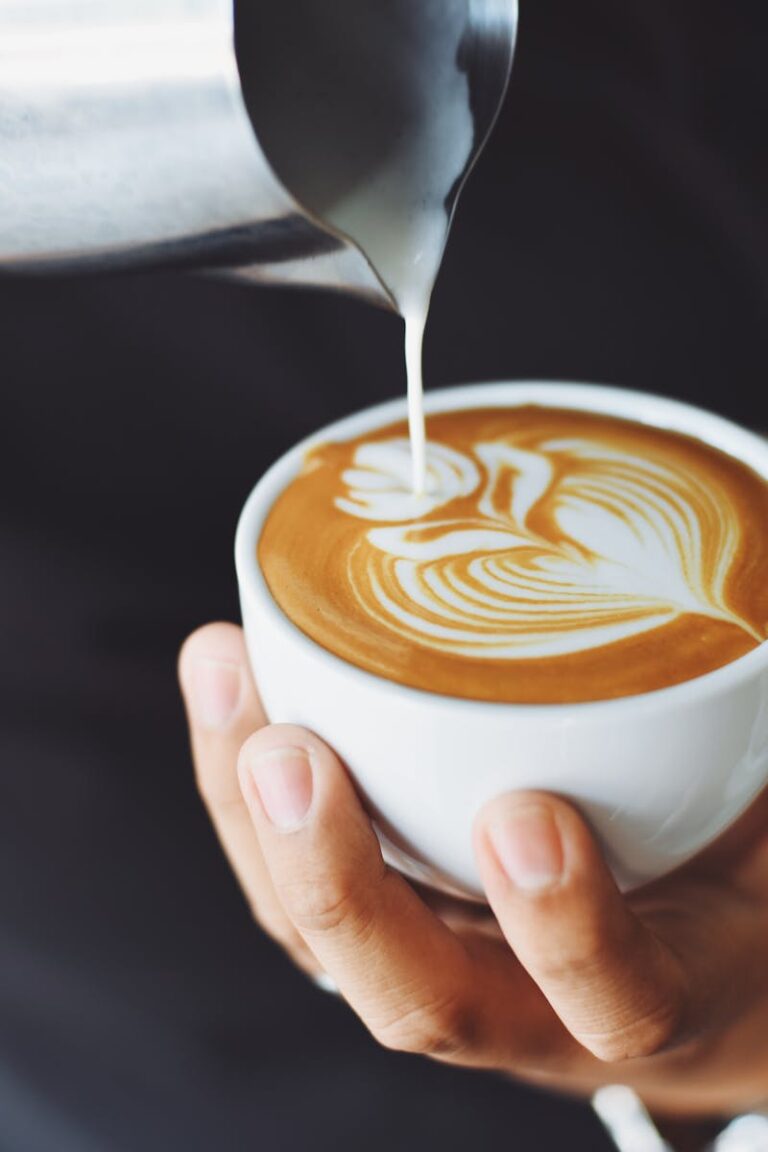 Close-up of a barista pouring milk to create latte art in a coffee cup.