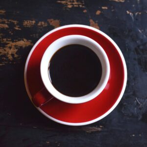 Top view of red ceramic cup of hot aromatic black coffee with saucer placed on shabby wooden table