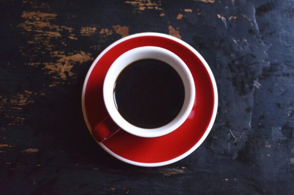 Top view of red ceramic cup of hot aromatic black coffee with saucer placed on shabby wooden table