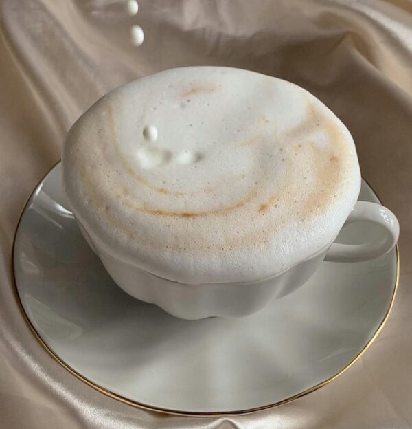 Delicate cappuccino topped with foam as milk pours, set against luxurious satin fabric.