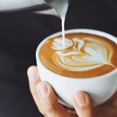 Close-up of a barista pouring milk to create latte art in a coffee cup.