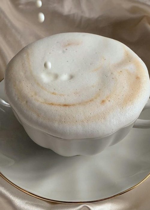 Delicate cappuccino topped with foam as milk pours, set against luxurious satin fabric.